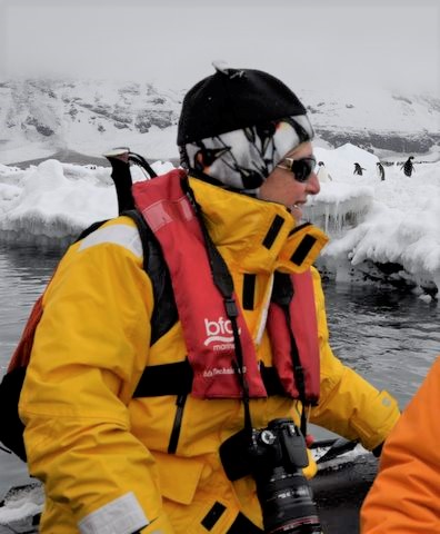 Woman in cold weather clothing, sitting on a boat in the middle of an ice pack with penguins in the background. Woman in cold weather clothing, sitting on a boat in the middle of an ice pack with penguins in the background.