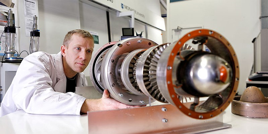Person in white lab coat looking at complex circular metal components. Person in white lab coat looking at complex circular metal components.