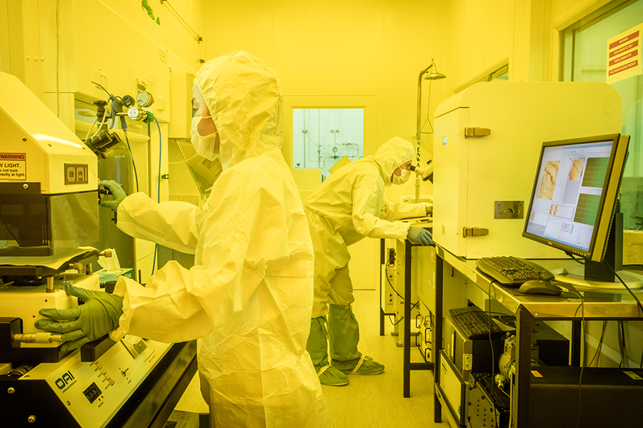 Image shows 2 scientists wearing protective lab clothing, working with laboratory equipment.