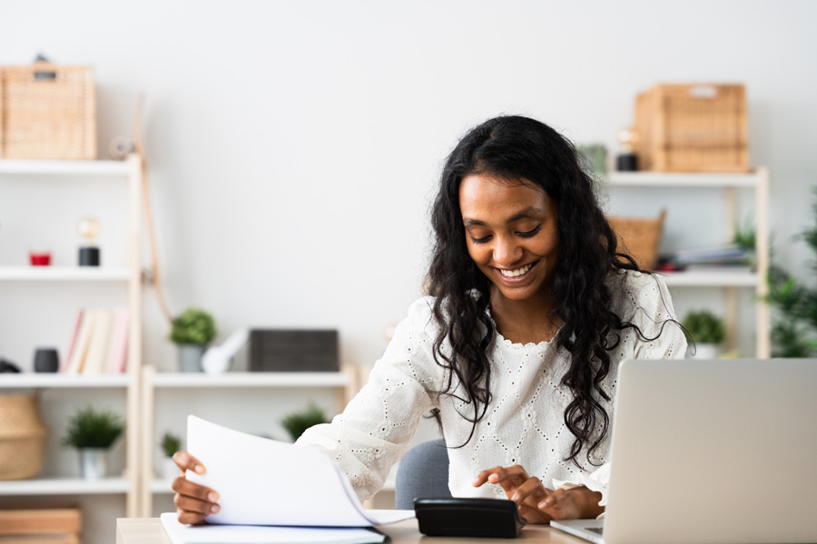 An Indian woman at a desk using a calculator while reading some documents.