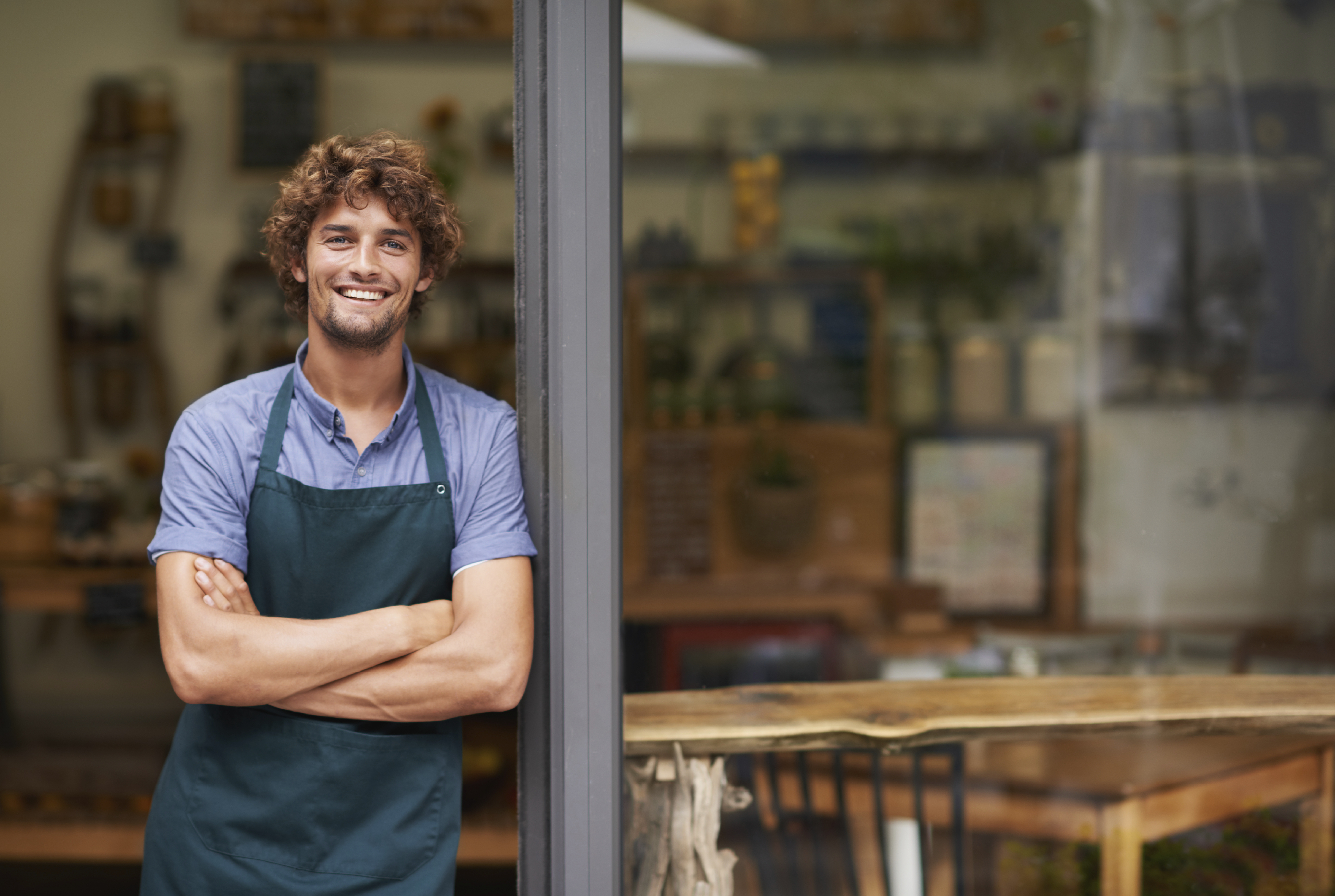 Smiling man wearing an apron standing outside a cafe